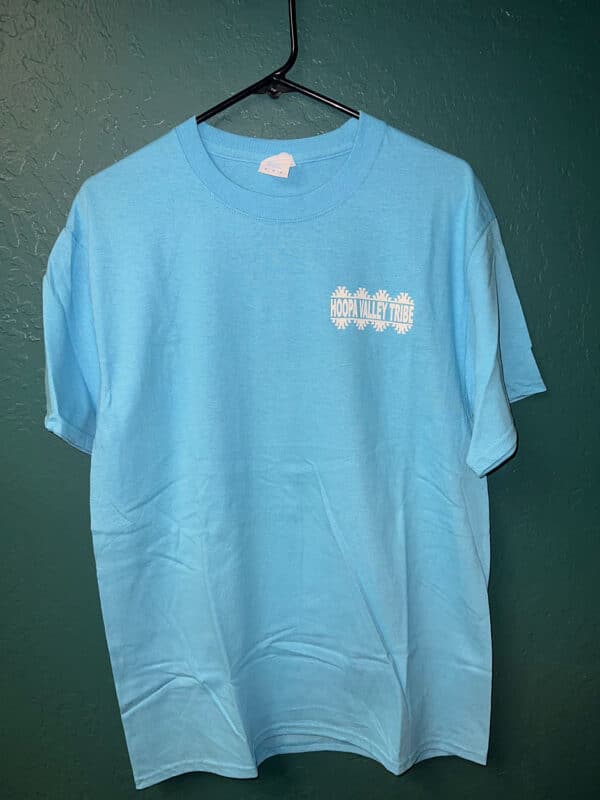A baby blue tshirt hangs on a wall hook, with the Hoopa Valley Tribe logo visible