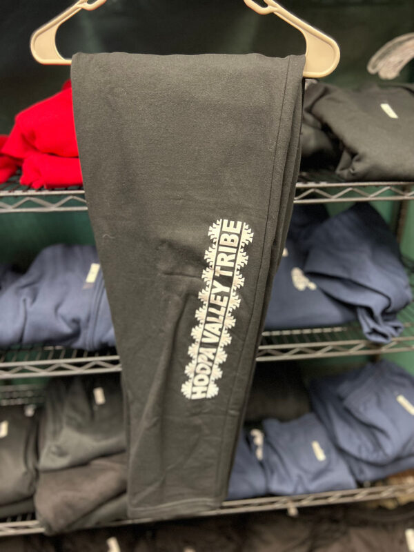 A pair of black sweatpants with the Hoopa Valley Tribe showing hangs on a rack.