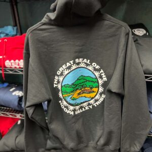 A black hooded jacket hangs on a rack, with the Hoopa Valley Tribe logo showing