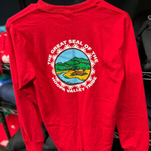 A red long-sleeve t-shirt hangs on a rack with the Hoopa Valley Tribe logo showing