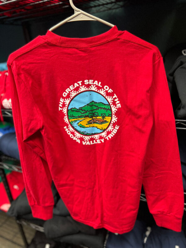 A red long-sleeve t-shirt hangs on a rack with the Hoopa Valley Tribe logo showing