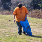 Kid holding a bag in the middle of a field cleaning up trash