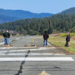 There are two people in the middle of a road and one person on a patch of grass