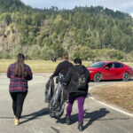 two people are carrying trash bags in the middle of a road while one person follows