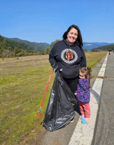 a adult and a kid are standing next to each other while holding a trash bag