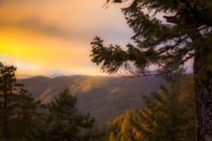 A view across a valley at sunset. The clouds and hills are lit in a bright golden light.