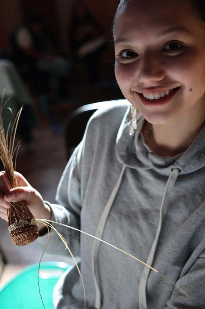 A smiling girl holds a partially-woven basket