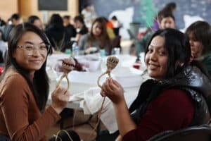 Two smiling people hold traditional woven baby rattles.